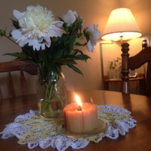 flowers and a lit beeswax candle on a crocheted doily on a kitchen table