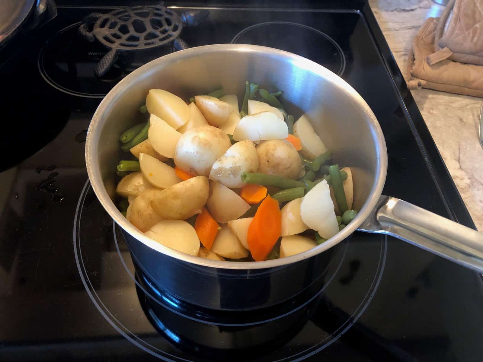 green beans, carrots and new potatoes in a stainless steel pot on the stove