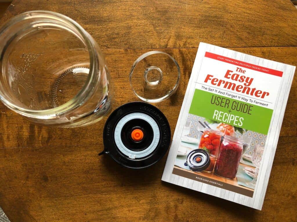 mason jar, fermentation lid, glass fermentation weight and recipe book on a wooden table