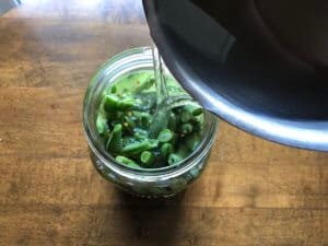 pouring salt brine from a pot into a jar of green beans