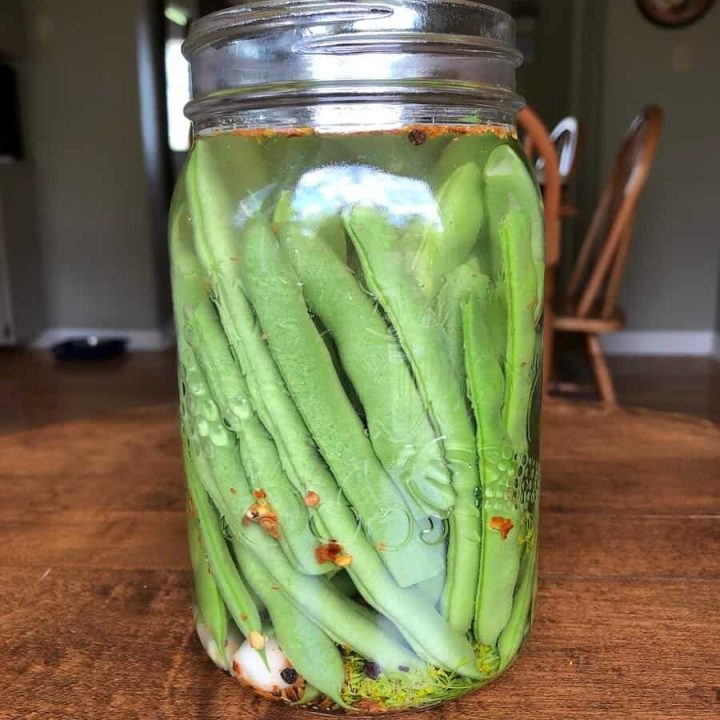 side view of green beans in a mason jar in brine with spices