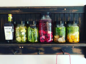 Fermented cucumbers, green beans, beets, sweet peppers, and cherry tomatoes, in mason jars, lined up on a shelf.