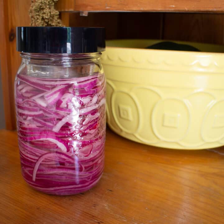 Jar of red onions in brine next to a bright yellow fruit bowl