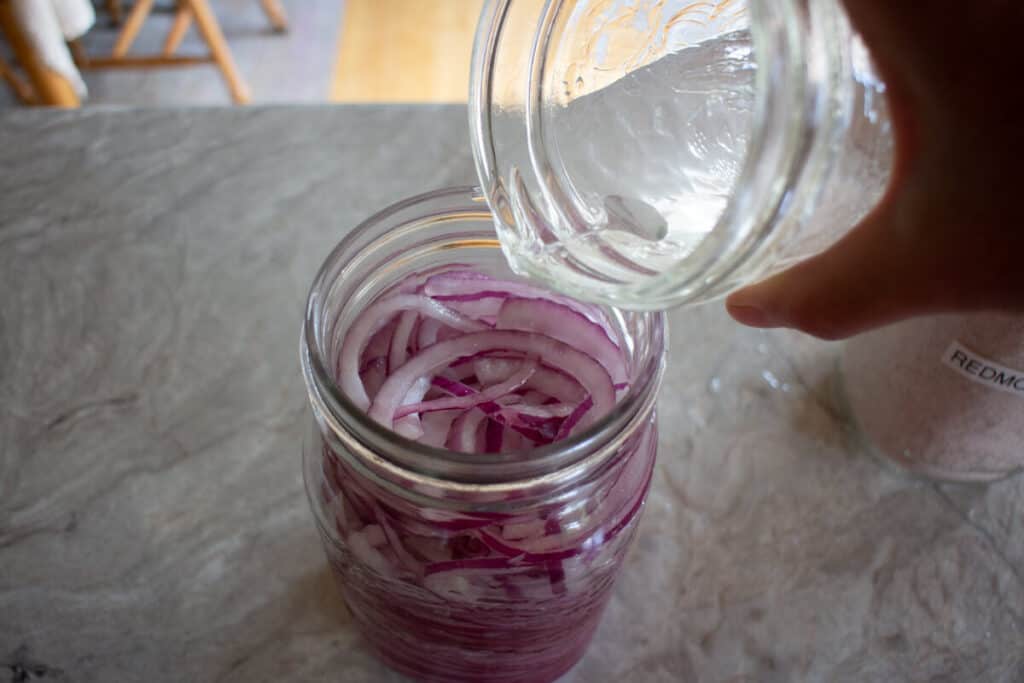Pouring brine over jar of sliced red onions