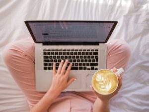 woman sitting cross legged with laptop and coffee on her lap