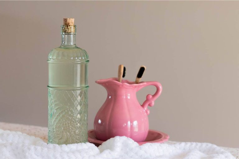 green glass bottle of homemade mouthwash, pink pitcher with bamboo toothbrushes