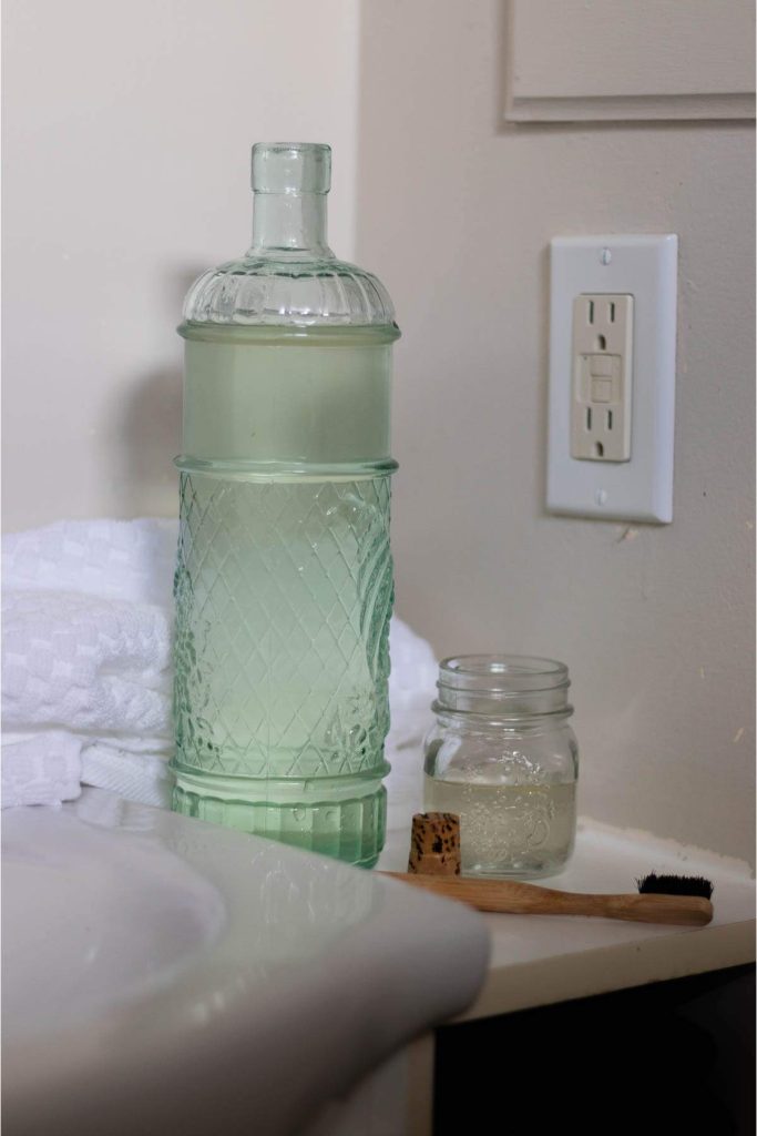 green glass bottle of mouthwash, a small jar and a bamboo toothbrush in a bathroom