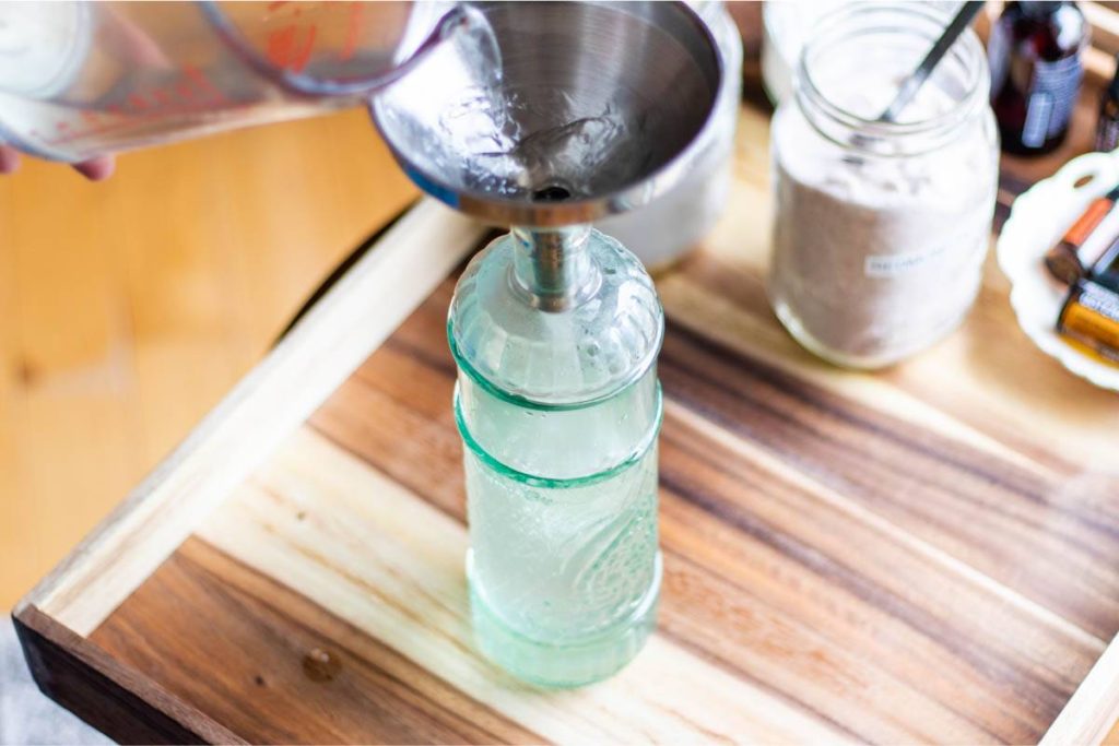 funnel in a green glass bottle, homemade mouthwash being poured in